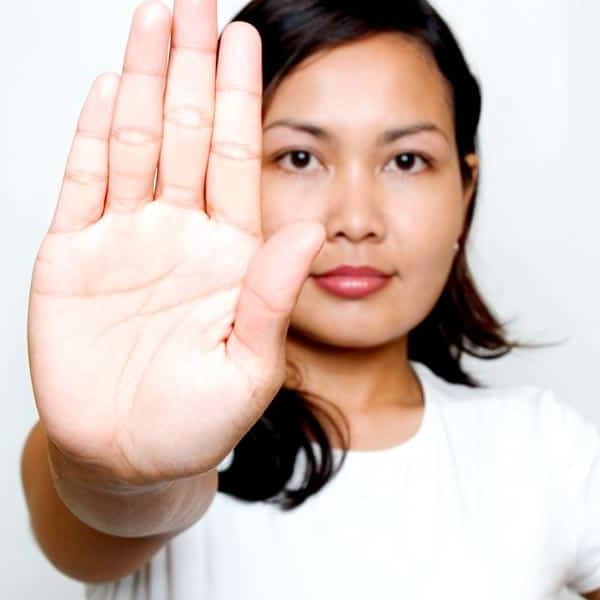 young woman in white shirt holding up hand defensively to back off
