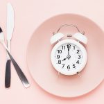 fasting theme with plate and alarm clock on pink background